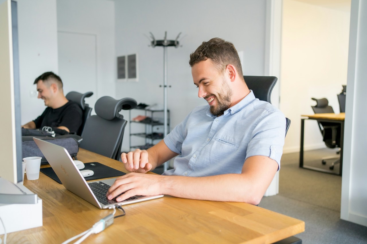 Two males working at desk smiling at laptop