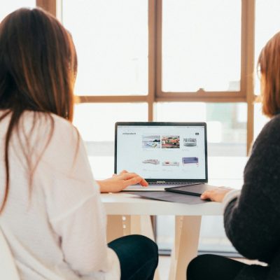 Two females working on one laptop facing away from us
