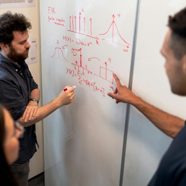 Two males and one female at a whiteboard drawing a diagram